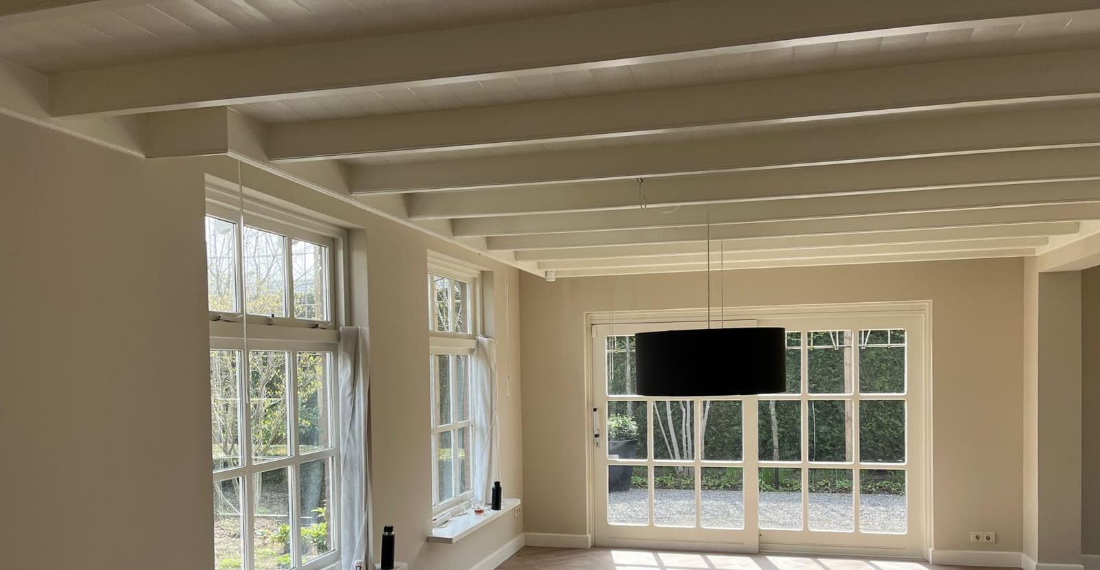 Woonkamer met wit geschilderd balkenplafond, kozijnen en openslaande tuindeuren